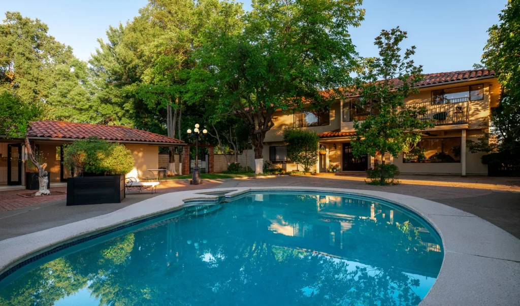 Swimming pool surrounded by mature trees and landscaping.